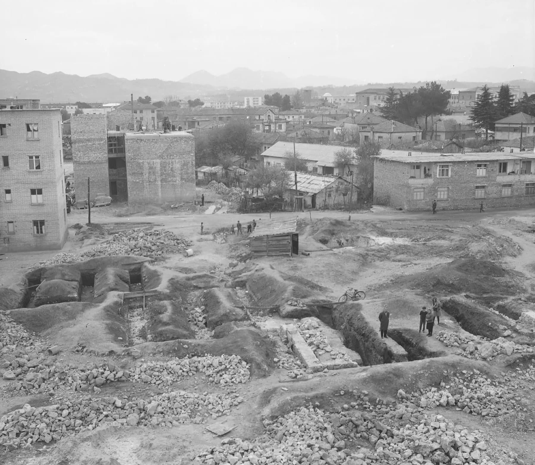 Black-and-white 1972 photograph of the excavation in the Partizani block of Tirana, with residential buildings behind the dig.